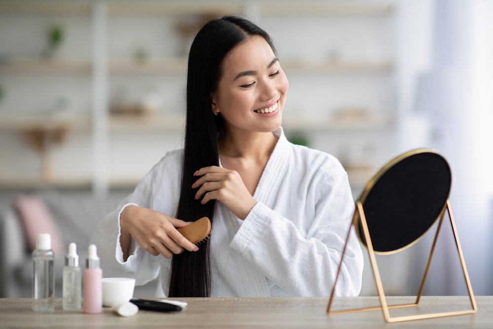 Cheerful,Young,Asian,Lady,In,Bathrobe,Sitting,In,Bedroom,,Combing